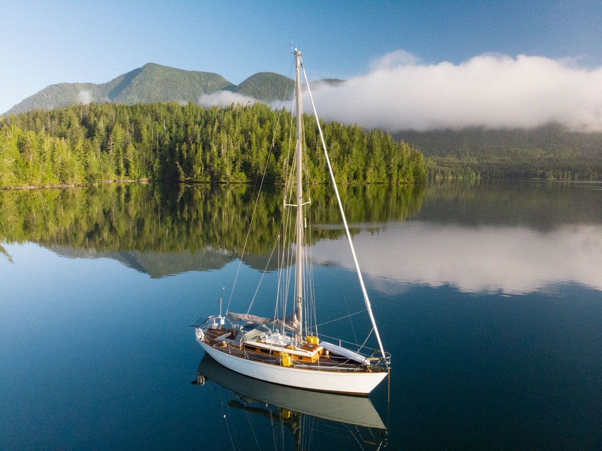 Jura at anchor on still water, with mist on the forested hills behind her